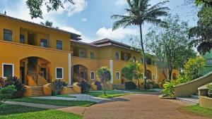 a large yellow building with a palm tree at Mercure Goa Devaaya Resort in Old Goa