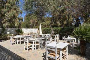 a patio with white tables and chairs and a tree at Surfing Beach Village Paros in Santa Maria