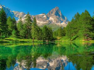 a reflection of a mountain in a lake with trees at Hotel Marmore in Breuil-Cervinia