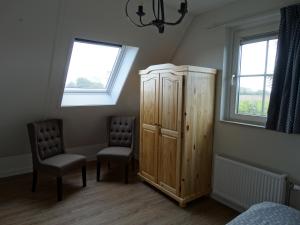 a bedroom with a wooden cabinet and two chairs at Vakantiehuis het Neerland in Biggekerke