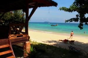 a man walking on a beach with a boat in the ocean at Phi Phi Relax Beach Resort in Phi Phi Islands