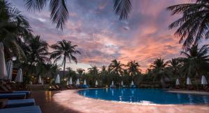 a resort pool with palm trees and a sunset at Blue Ocean Resort in Mui Ne