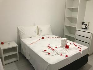 Una cama blanca con pétalos de rosa roja. en Porto Luar, en Porto Seguro