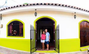 dos personas de pie en la puerta de una casa amarilla y blanca en Casa Lula León Hostal, en León