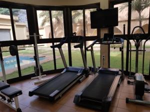 a gym with treadmills and a tv and windows at Hotel la Coccinelle in Bamako