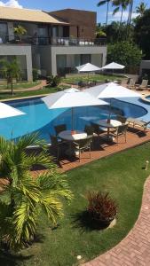 a pool with tables and umbrellas next to a building at Condomínio Solaris Imbassai in Imbassai