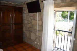 Habitación con ventana y TV en una pared de piedra. en Casa Loureiro en Caldas de Reis