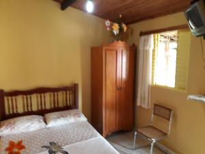 1 dormitorio con 1 cama, TV y silla en Suítes Dona Ilda, en Pirenópolis