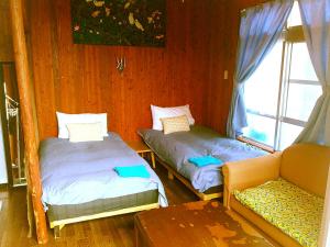 2 łóżka w pokoju z kanapą i oknem w obiekcie Guest House Miyakojima w mieście Miyako-jima
