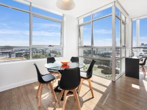 a dining room with a table and chairs and windows at As the Sun Sets - Modern and Spacious 2BR Zetland Apartment Facing the Setting Sun in Sydney