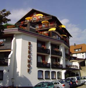 バイアースブロンにあるPanoramahotel Berghofのバルコニー付きの大きな建物、駐車場に駐車した車