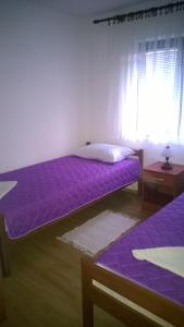two beds in a room with purple sheets and a window at Apartman Dolac in Karlobag