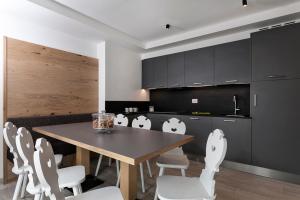 Una cocina con una mesa de madera y sillas blancas. en Appartamento Fuoco, en Andalo