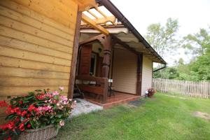 a wooden cabin with a porch with flowers in the yard at U Kaczorka in Ruciane-Nida