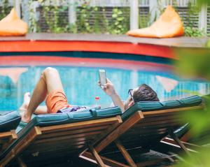 a person laying in front of a pool holding a cell phone at Grandmas Plus Hotel Seminyak in Seminyak