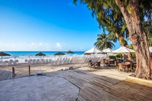 a beach with tables and umbrellas and the ocean at Bougainvillea Barbados in Christ Church