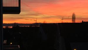 einen Blick auf den Sonnenuntergang über einer Stadt mit Windturbinen in der Unterkunft ZISA Ferienwohnung Bodensee in Friedrichshafen