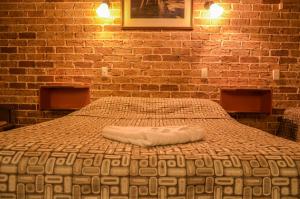 Cama en habitación con pared de ladrillo en Beenleigh Village Motel, en Beenleigh