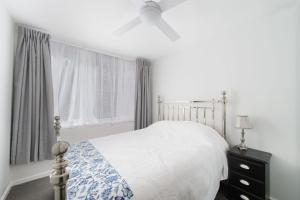 a white bedroom with a bed and a ceiling fan at Flynns Beach Apartments 4 41 Pacific Drive in Port Macquarie