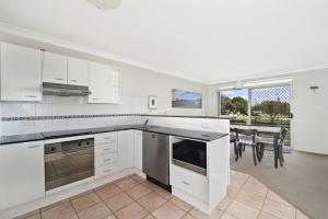 a kitchen with white cabinets and a dining room with a table at Westport Palms 14 Buller Street in Port Macquarie