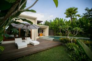 una terraza de madera con sillas y una sombrilla junto a la piscina en Senetan Villas and Spa Resort, en Payangan