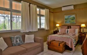ein Schlafzimmer mit einem Bett, einem Sofa und Fenstern in der Unterkunft Muchenje Self Catering Cottages in Chobe