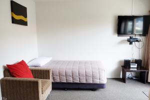 a bedroom with a bed and a chair and a tv at Marksman Motor Inn in Wellington