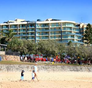 une famille marchant sur la plage avec un hôtel en arrière-plan dans l'établissement Landmark Resort, à Mooloolaba