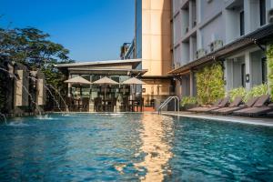 a swimming pool in front of a building with chairs at Nouvo City Hotel in Bangkok