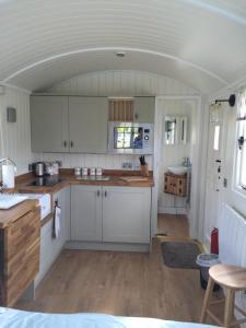 a kitchen with white cabinets and a wooden floor at Weatherhead Farm Shepherds Hut in Buckingham