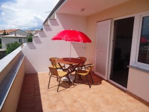 a table and chairs on a balcony with a red umbrella at Apartments Ante in Senj