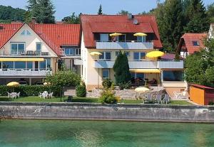 a house with chairs and umbrellas next to the water at Gästehaus am Bodensee in Immenstaad am Bodensee
