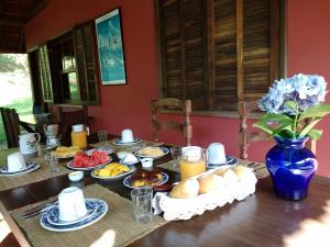 uma mesa com comida para o pequeno almoço e um vaso azul com flores em Pousada das Fadas em Visconde de Mauá