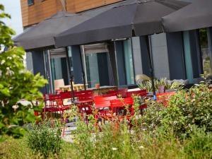 a group of red tables and chairs under an umbrella at ibis Lyon Est Meyzieu in Meyzieu