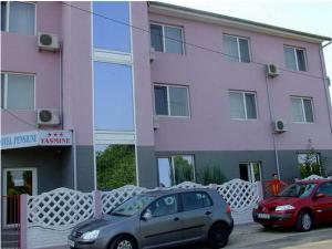 two cars parked in front of a pink building at Pension Yasmine in Timişoara