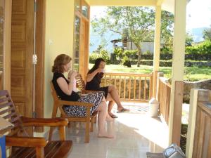 Dos mujeres sentadas en el porche de una casa en Lembah Rinjani Villa & Resto by ecommerceloka, en Sembalun Lawang