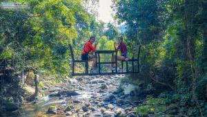 duas mulheres sentadas numa ponte suspensa sobre um rio em Namkat Yorla Pa Resort em Ban Kat