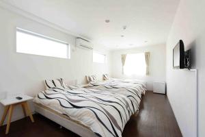 a white bedroom with a large bed with striped sheets at Shima Stay holoholo in Zamami