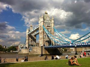 a suspension bridge with people sitting on the grass in front of it at Charming London Town Studio Flat, Tower Bridge in London