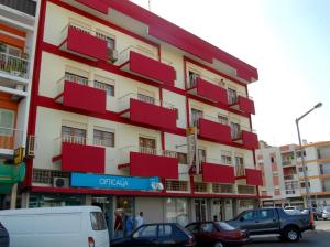 un edificio rosso e bianco con macchine parcheggiate di fronte di Aparthotel Avenida a Mindelo