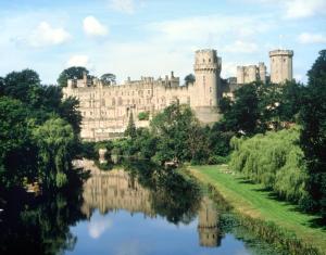 a castle with a river in front of it at Mousley House Farm Campsite and Glamping in Warwick