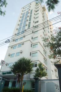 um edifício alto e branco com palmeiras em frente em Ímpar Suítes Cidade Nova em Belo Horizonte