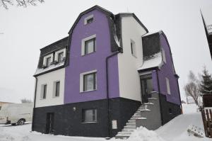 une maison violette et blanche dans la neige dans l'établissement Apartments Villa Viola, à Kovářská