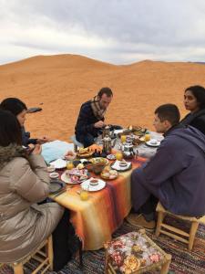 un grupo de personas sentadas alrededor de una mesa en el desierto en Sahara camel tours camp, en Merzouga