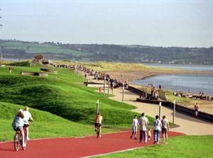 a group of people walking and riding bikes on a path near a beach at Renovated Church close to the beach in Llanelli