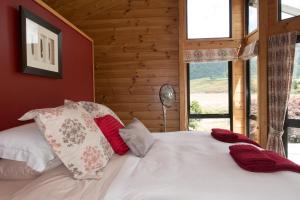 Un dormitorio con una cama blanca con almohadas rojas y blancas en Astelia Lodge, en Horohoro