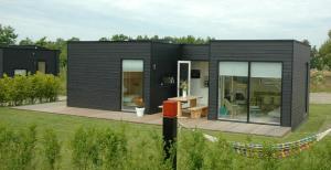 una pequeña casa negra con terraza de madera en Wadzand, en Midsland