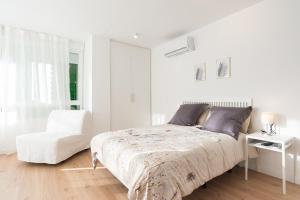 a white bedroom with a bed and a white chair at Estudio Playa Candado in Málaga