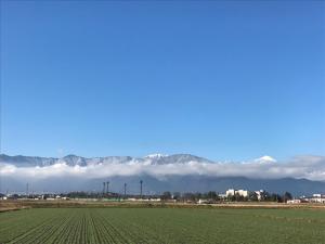 a field with mountains in the background with clouds at EN Guest house in Matsumoto