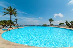 a large blue swimming pool next to a beach at Alua Calas de Mallorca Resort in Calas de Mallorca